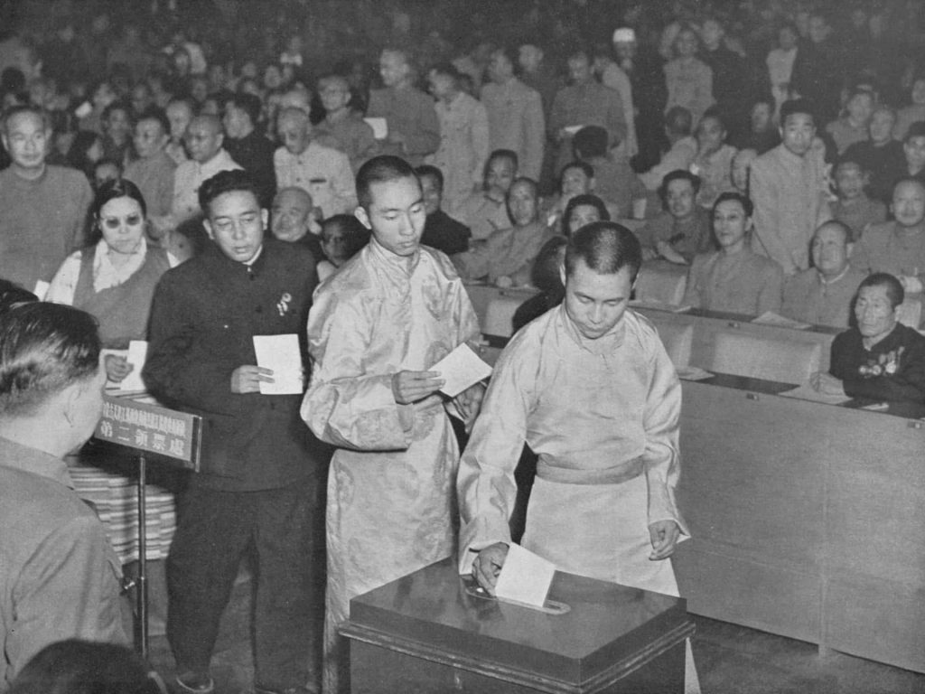 At the first National People’s Congress of the People’s Republic of China, the Dalai Lama and Panchen Lama cast their votes for the Constitution amidst political pressures. © Public Domain